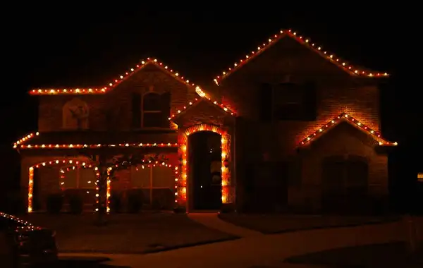 Two-story brick home with roofline, gables and arched entry outlined in red and warm white lights at night