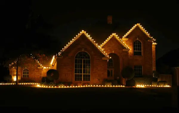Brick home at night with gables outlined in warm white lights and a lit string along the front ground line
