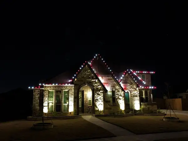Stone and brick home at night with roofline outlined in alternating red and white lights and uplighting on the stonework