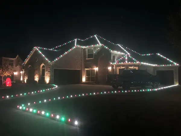 Brick home at night with roofline and driveway edge outlined in alternating red, green and white bulbs