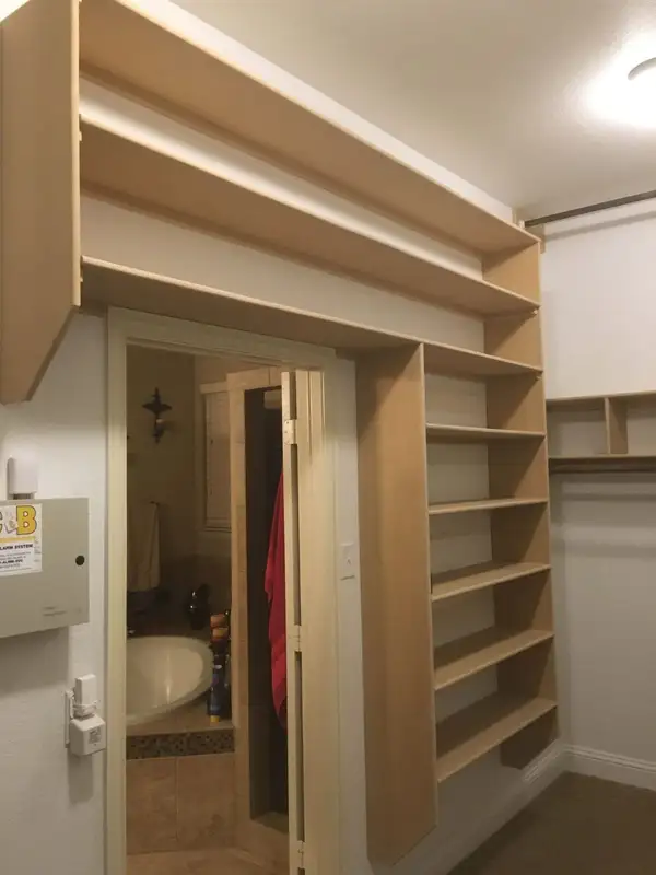 Unfinished built-in closet shelving above a bathroom doorway in a walk-in closet
