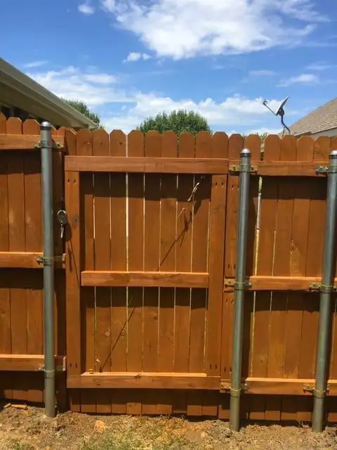 Stained wood privacy fence gate hung between galvanized steel posts