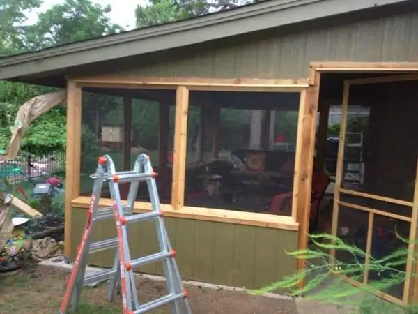 Wood framing for a screened porch enclosure on a green-sided building, with a ladder