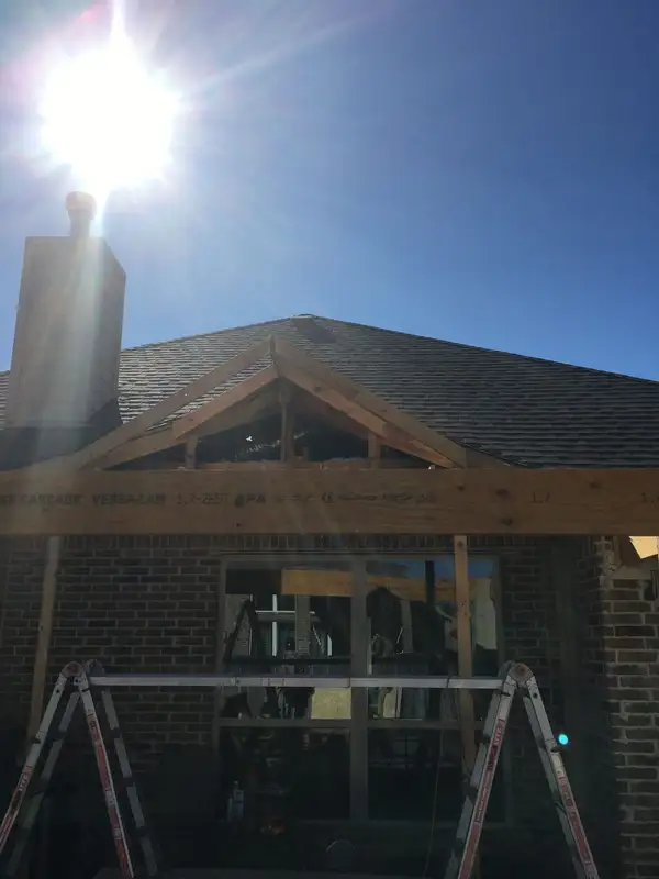 Gabled roof framing for a new patio cover on a brick home, backlit by the sun