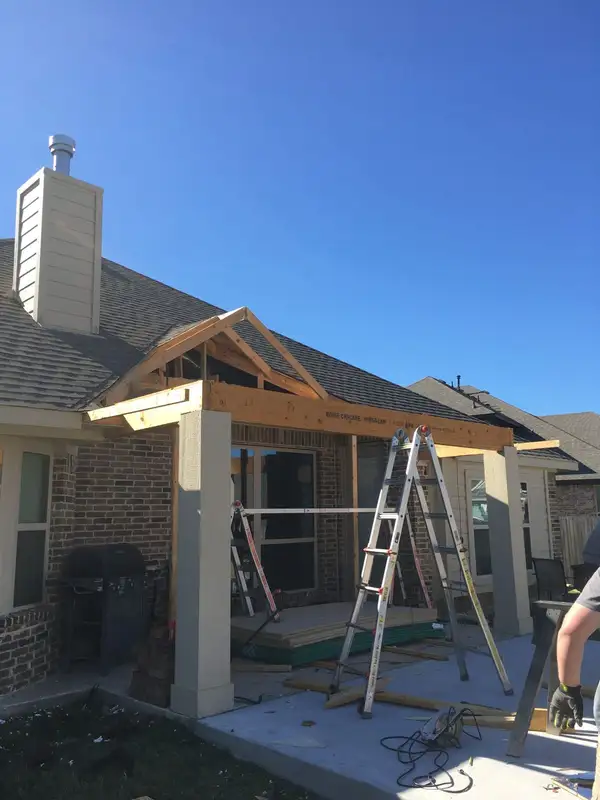 Framing for a gabled patio cover with square columns off the back of a brick home