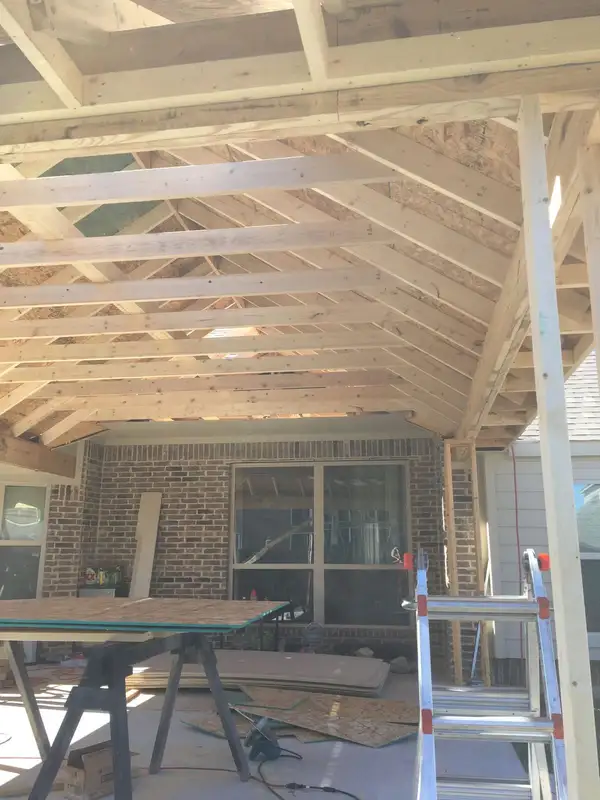 Roof rafters and decking under construction inside a patio cover attached to a brick home