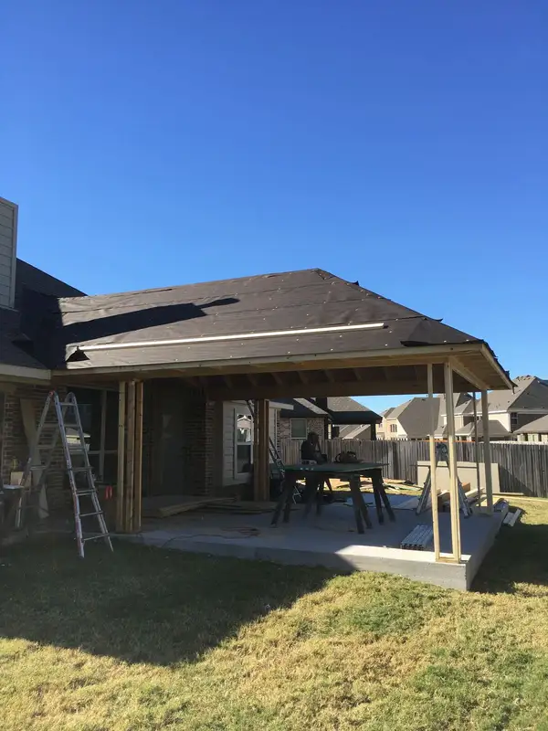 Hip-roof patio cover framing with roofing underlayment installed, attached to the back of a brick home