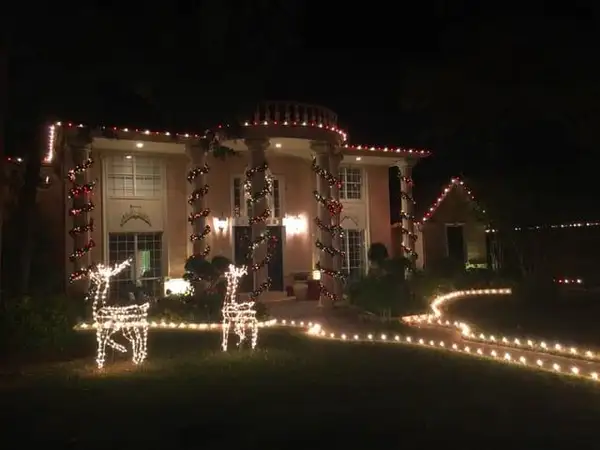 Two-story home with red and white lights spiraling around columns, lit reindeer figures and a warm white lit walkway