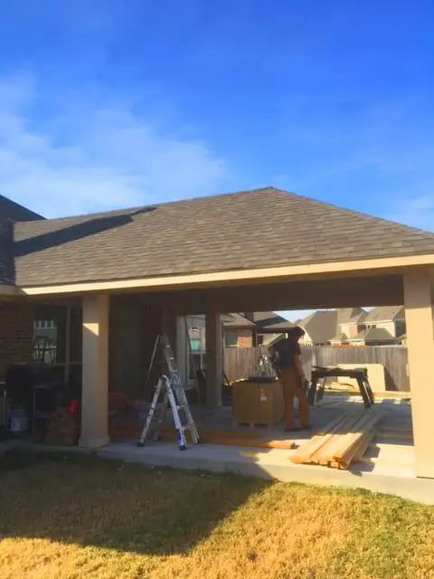 Hip-roof patio cover with shingles and square columns over a concrete patio, nearing completion