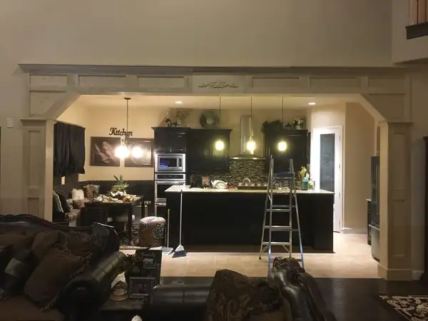 Interior opening between living room and kitchen framed with unfinished paneled wood trim and columns