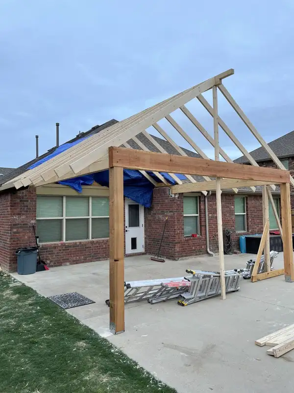Gable patio cover under construction with cedar post and beam, new rafters and a tarp over the roof opening