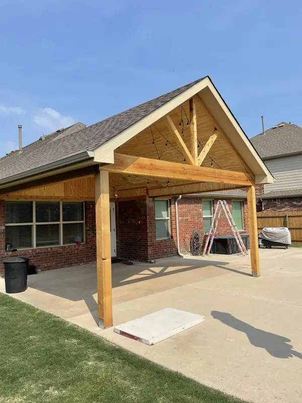 Finished gable patio cover with cedar posts, plywood ceiling and string lights over a concrete patio at a brick home