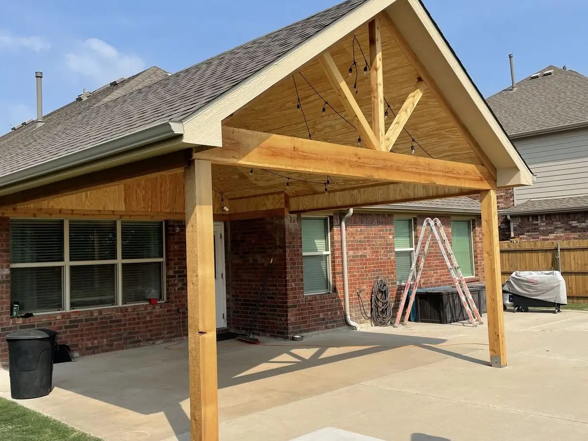 Finished gable patio cover with cedar posts, plywood ceiling and string lights over a concrete patio at a brick home