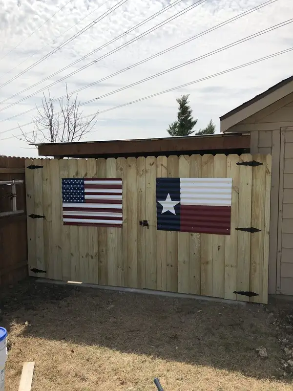 Wood privacy double gate with corrugated metal American and Texas flag panels beside a shed