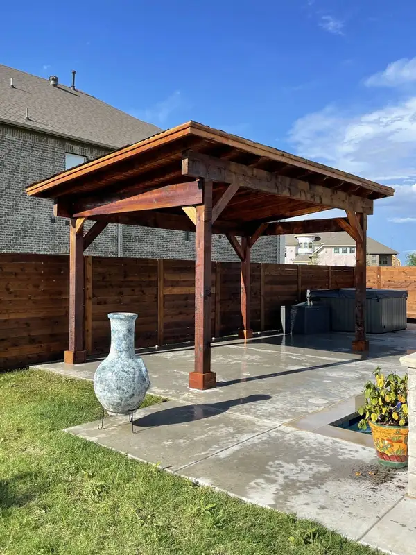 Freestanding stained cedar pavilion with heavy posts and knee braces over a concrete patio beside a hot tub