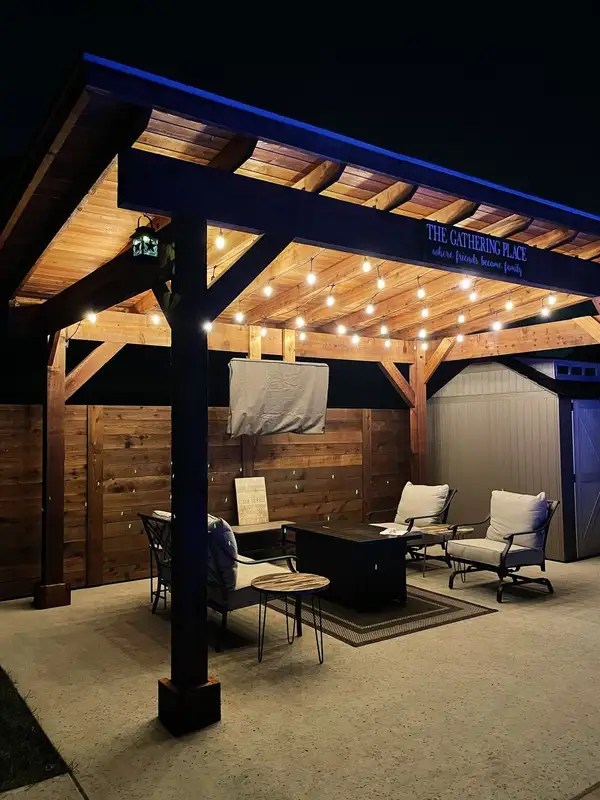 Cedar pavilion at night with string lights, a fire pit table and seating on a concrete patio