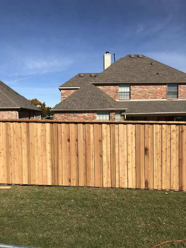 Cedar-tone board-on-board privacy fence with a cap rail along a backyard lawn
