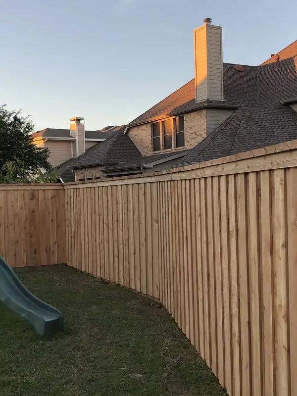 Cedar-tone board-on-board privacy fence with cap running along a backyard at sunset
