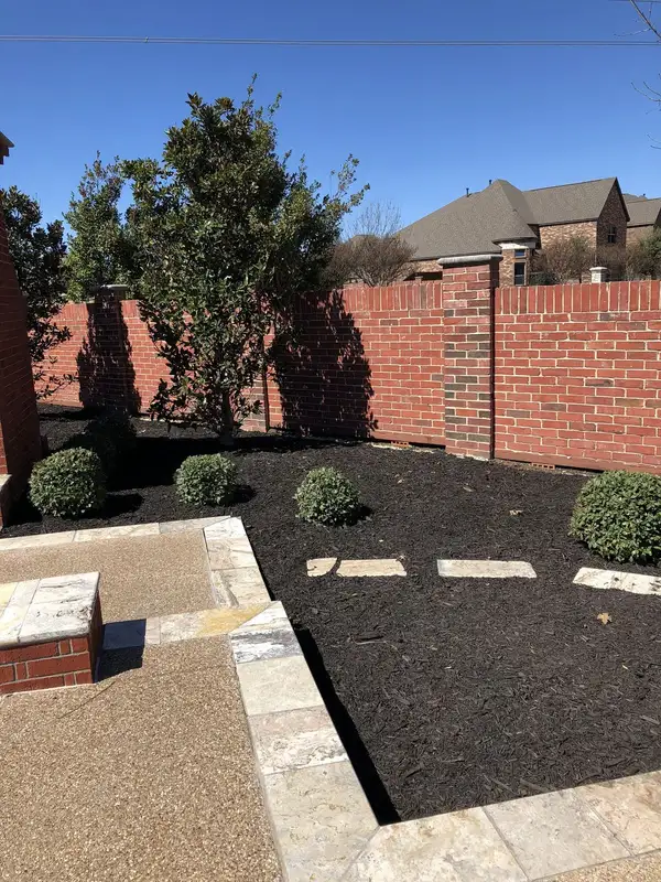 Backyard bed of fresh black mulch with round shrubs, stone edging and stepping stones beside an aggregate patio