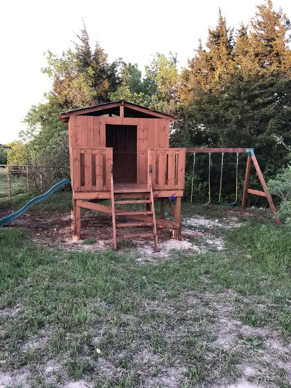 Finished stained wood playhouse on a raised platform with ladder, slide and swing set