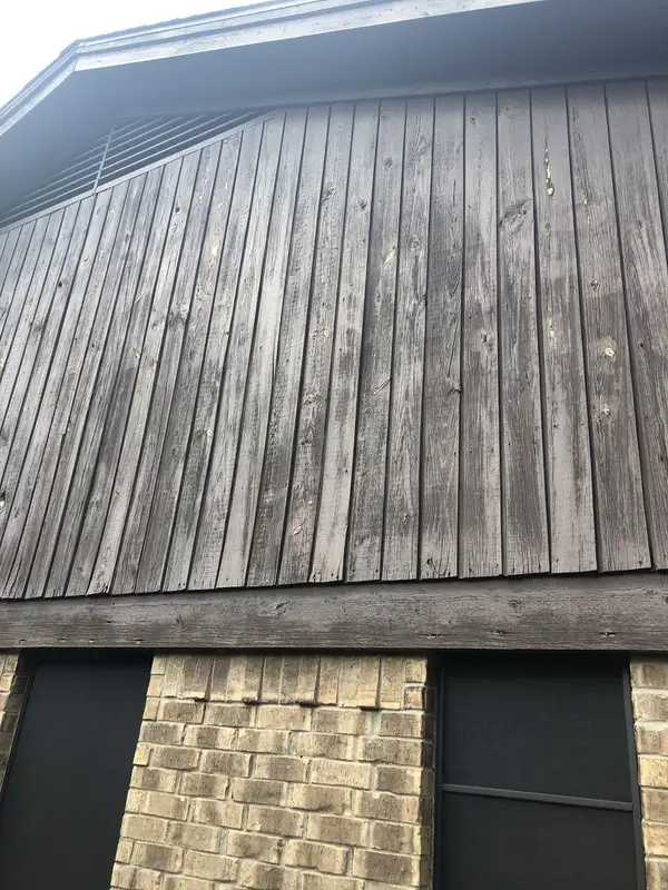 Weathered, graying vertical wood siding on a gable above a brick wall