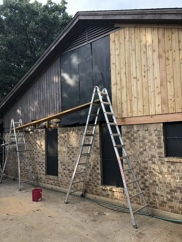 New vertical wood siding being installed on a gable over brick, with house wrap and ladders