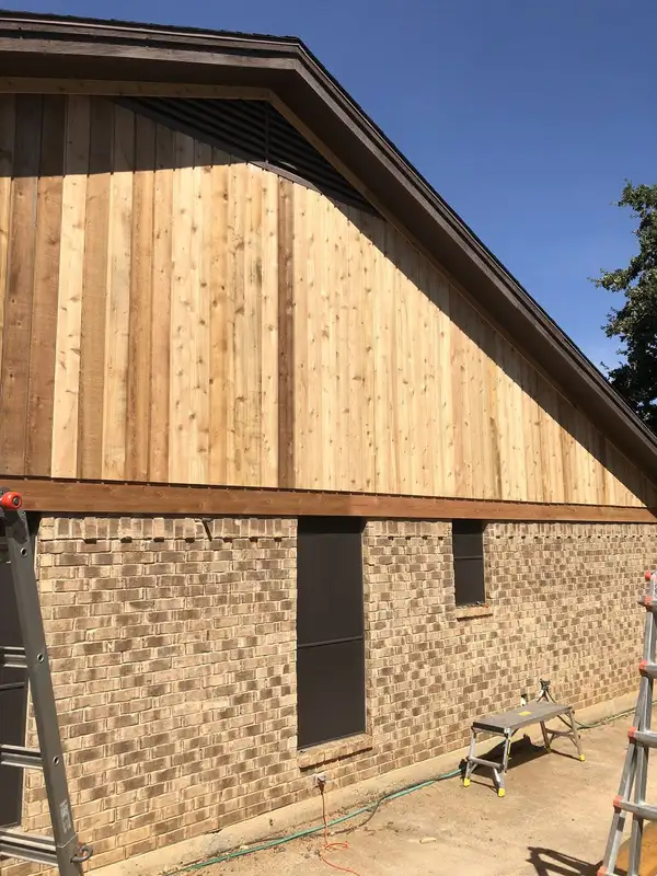 New unstained vertical wood siding covering a brick home's gable, with ladders at the edges