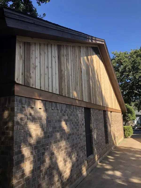 New vertical wood siding on the gable of a brick home, seen in late afternoon shade