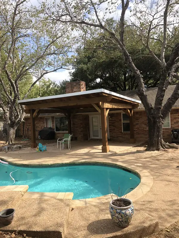 Stained wood patio cover with a low-slope white roof over a stamped concrete patio beside a pool