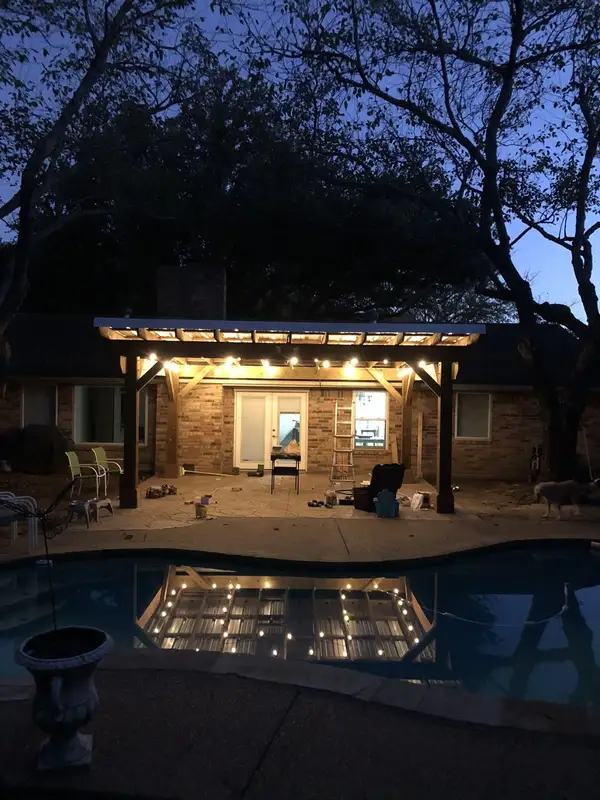 Patio cover with a corrugated metal roof lit by string lights at dusk, reflected in the pool
