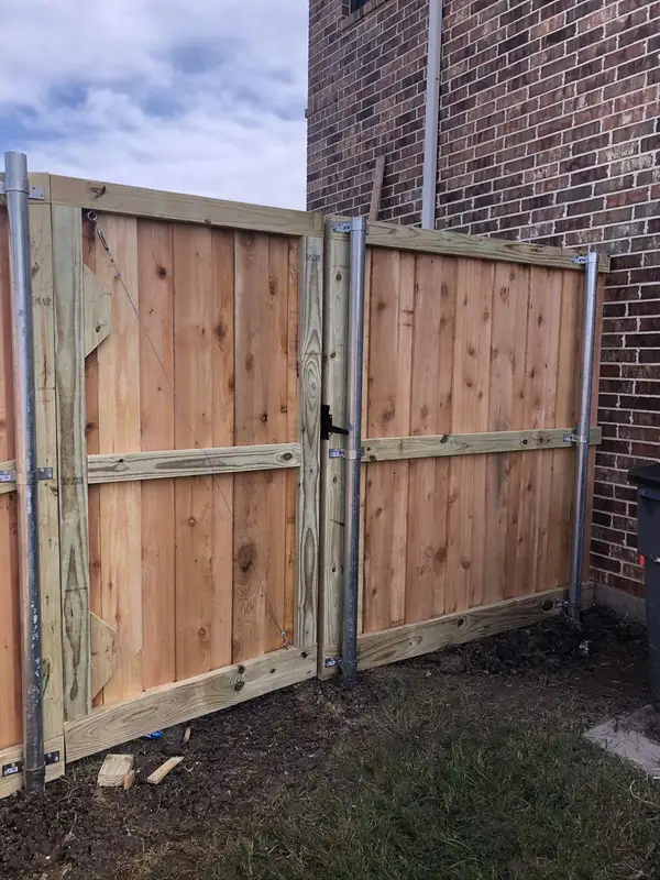 Cedar double gate with galvanized steel posts and diagonal cable bracing beside a brick home
