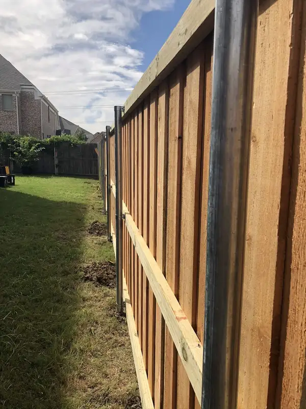 Cedar privacy fence under construction with galvanized steel posts and rails along a backyard
