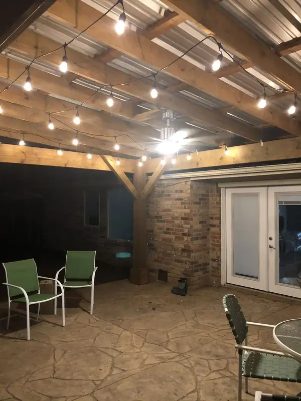 Covered patio with exposed wood beams, festoon string lights overhead and stamped concrete flooring at night