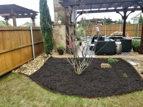 Backyard with a fresh mulch bed, rust-colored steel edging, a river rock strip, timber pergolas and a pool
