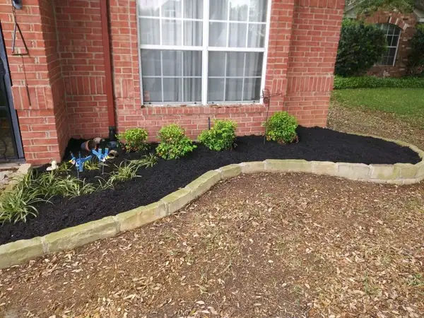 Curved bed edged with cut limestone blocks, fresh black mulch and small shrubs in front of a brick home