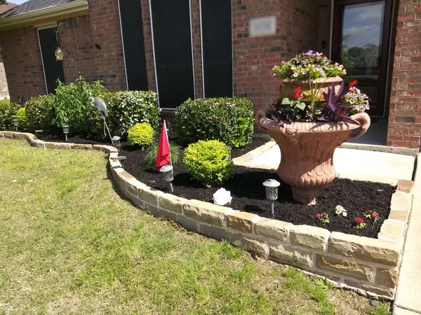 Raised front bed with stacked limestone block edging, fresh black mulch, shrubs and a flower urn