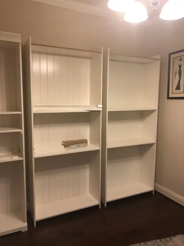 White bookcase units with beadboard-style backs standing along a wall in a room