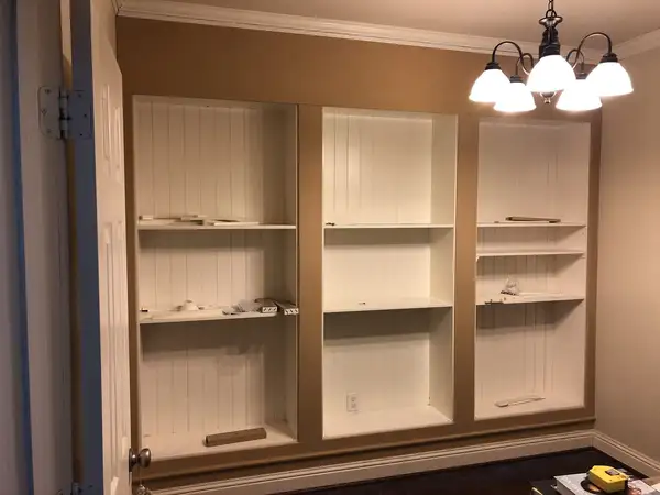 Built-in bookcase wall with beadboard-style backs framed by raw, unpainted trim boards