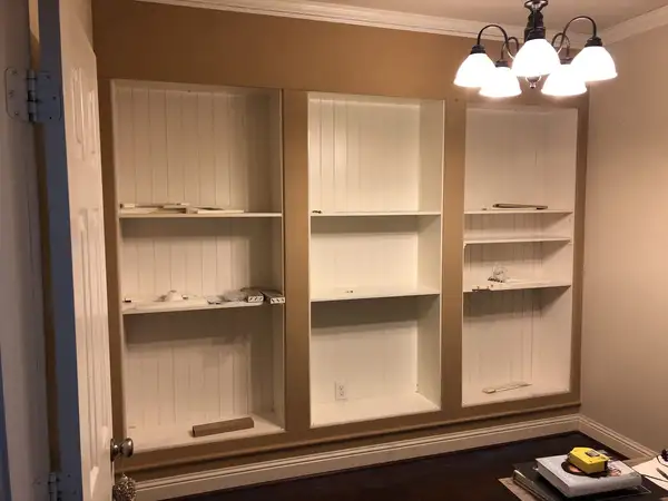 Three built-in bookcase bays framed with unpainted trim boards beneath a crown-molded ceiling