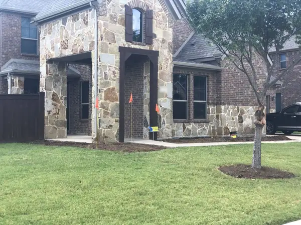 Stone and brick home with fresh soil beds, orange marking flags and a young tree in a soil ring