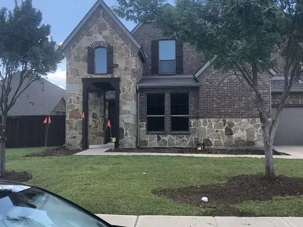 Fresh soil beds and orange marking flags along the front of a stone and brick home