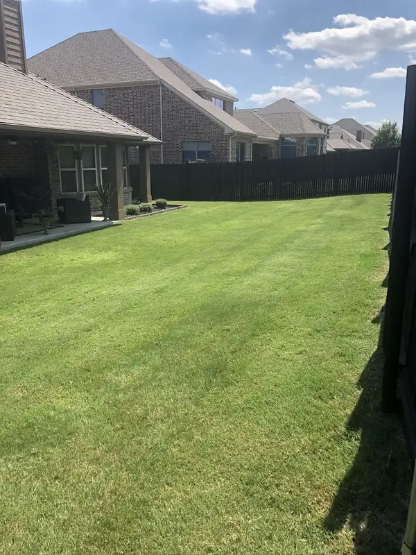 Freshly mowed backyard lawn beside a covered brick patio and a tall dark-stained fence