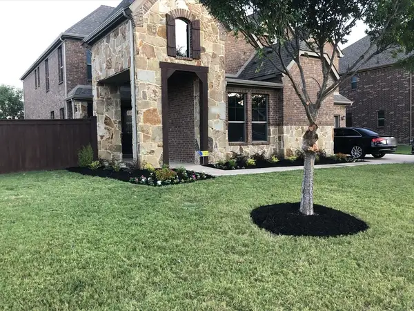 Freshly planted front beds with black mulch and flowers around a stone and brick home