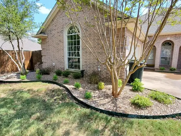 River rock bed with black steel edging, new shrubs and a crape myrtle beside a tan brick house