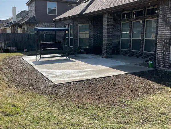 New concrete patio slab extending a covered brick patio, with raked bare soil around it